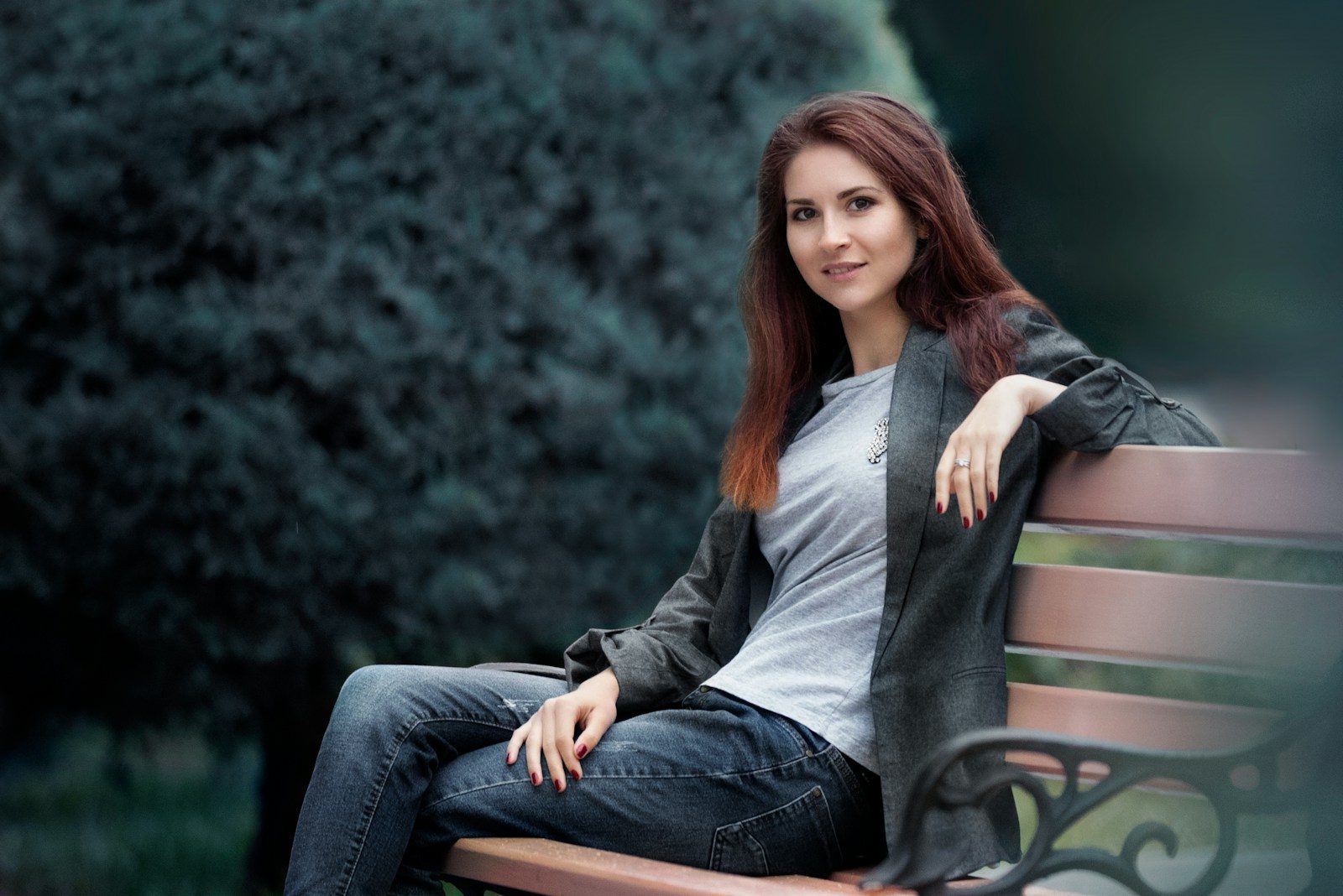 woman in gray long sleeve shirt and blue denim jeans sitting on green wooden bench